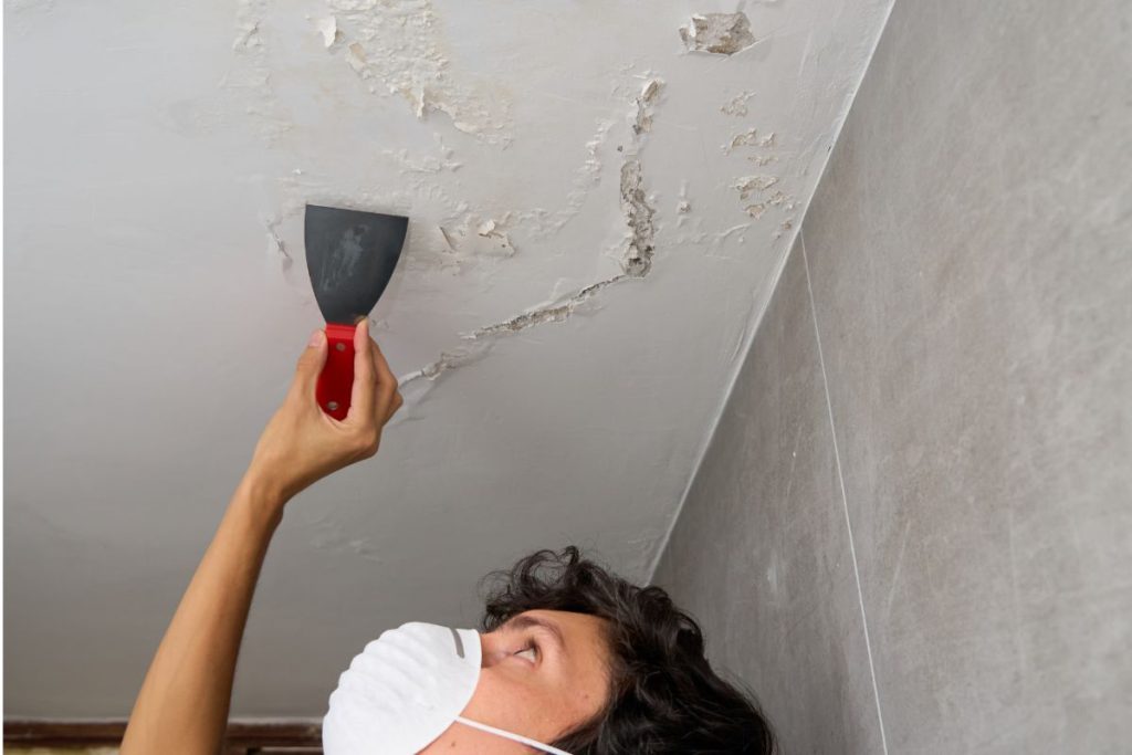 Hand pointing at bubbling paint on a damp ceiling under an upstairs bathroom